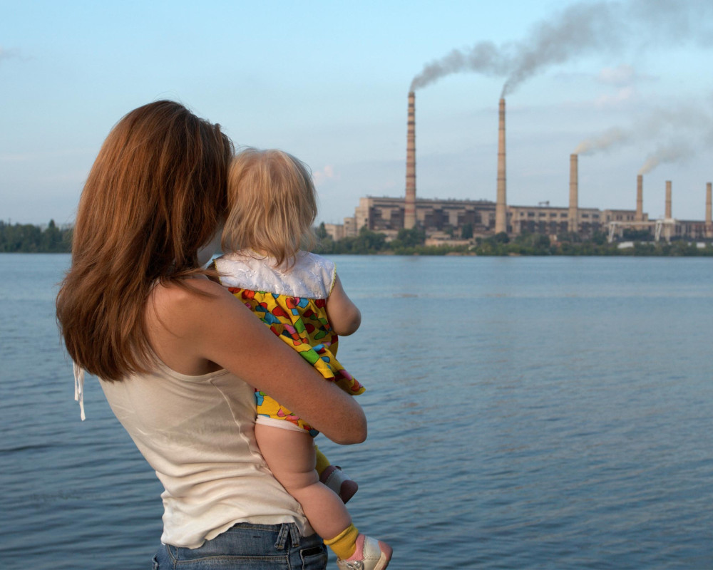 Woman holding child looking at factory smokestacks